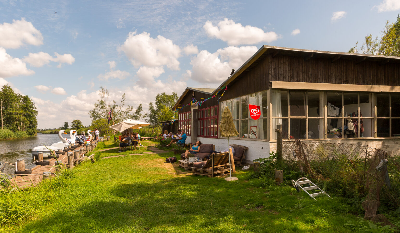 Blick auf die Peene mit schwanenförmigen Tretbooten, rechts der Gasthof Moorbauer